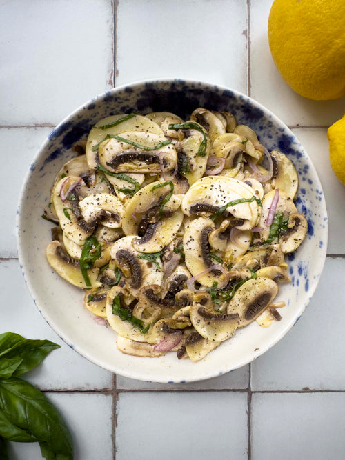 Raw mushroom salad with shallot, basil, black pepper and lemon in a speckled blue bowl