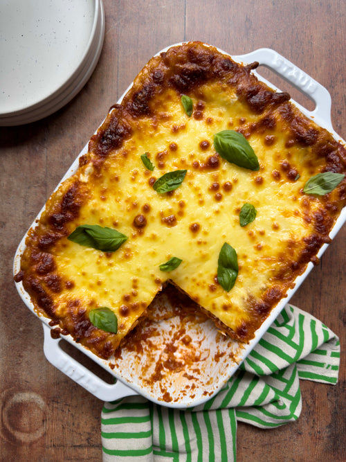 Baked lasagne topped with melted cheese and fresh basil in a white dish
