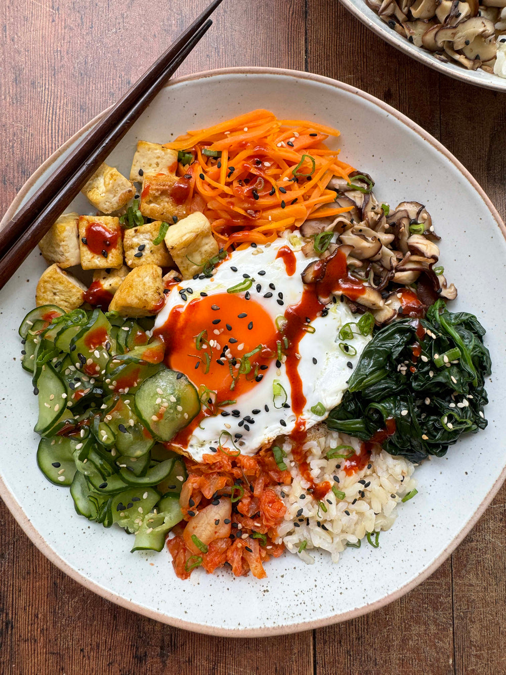 Brown rice bibimbap bowl with tofu, shiitake, kimchi, carrot, spinach and a fried egg